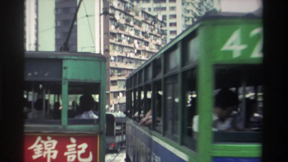 Green Hong Kong tram number 42 passes at close range; passengers visible through side windows; red Chinese shopfront sign and residential towers behind, circa 1982.