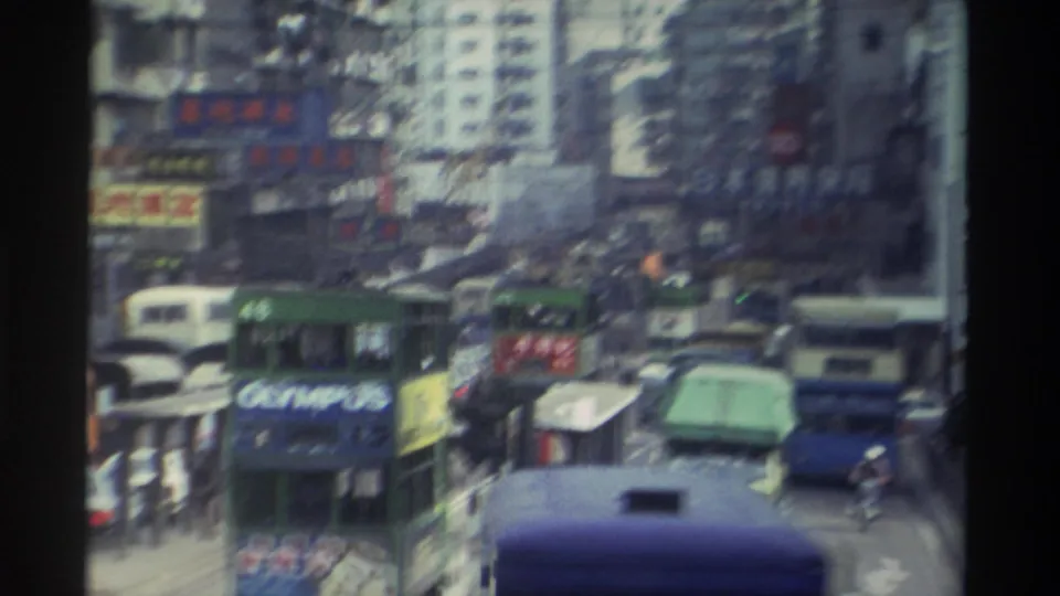 Wide street-level view of a congested Hong Kong thoroughfare with blue double-decker buses, a distant Olympus-branded vehicle, dense Chinese-language signage, and high-rise buildings, circa 1982.