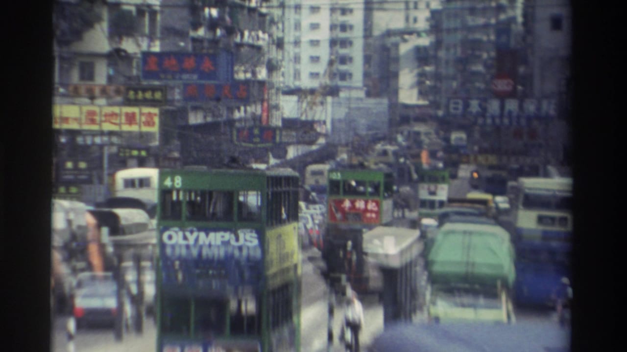 Green double-decker bus with Olympus advertisement in dense Hong Kong traffic, flanked by buildings covered in Chinese-character signs.
