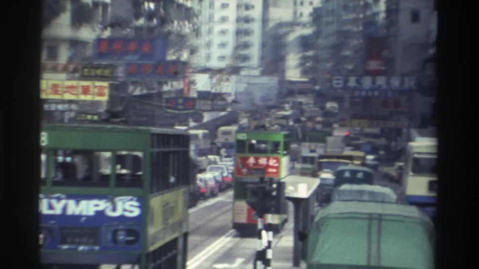 Green double-decker buses with a prominent Olympus advertisement fill a multi-lane Hong Kong street, 1982, with Chinese-character commercial signs densely covering tall apartment-block facades.