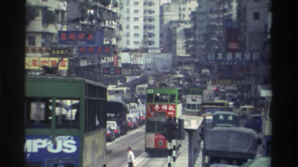 Green double-decker bus marked route 153 with Olympus advertisement in dense 1982 Hong Kong traffic, with Chinese-character signs on buildings and a pedestrian at street level, 8mm.