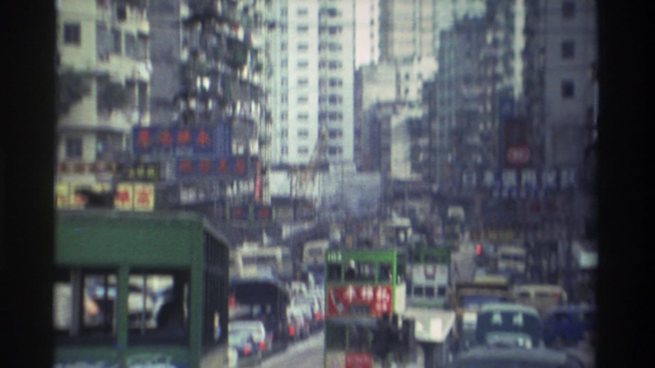 Dense Hong Kong street traffic seen through the frame of a green double-decker tram, with high-rise buildings and Chinese-character signs in the background.