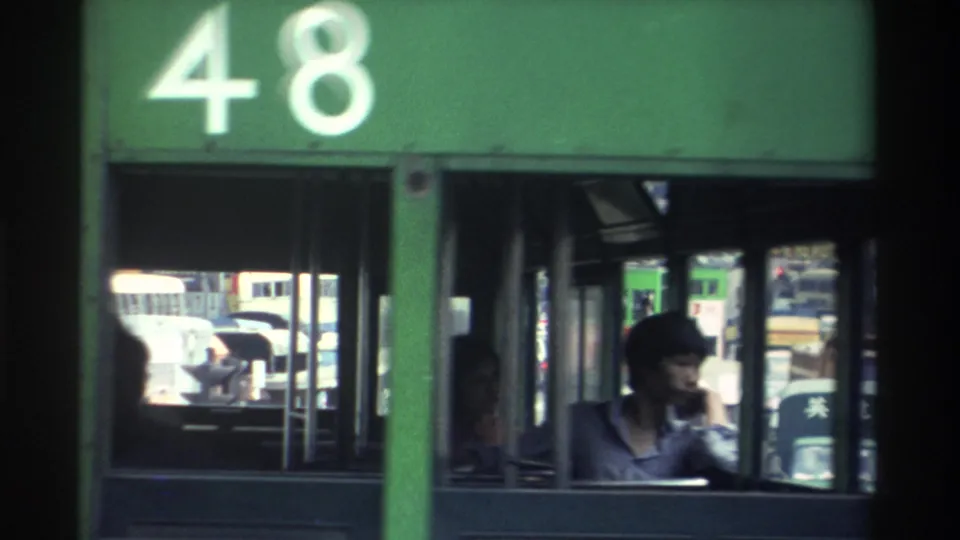 1982 Hong Kong: green double-decker tram showing route number 48; a capped figure is visible through the lower-deck window with dense traffic behind.
