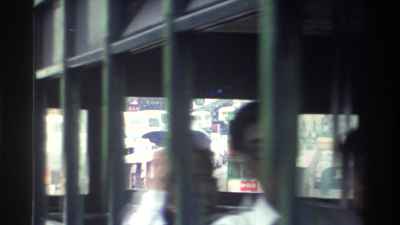 A man in a light collared shirt near the bus window; Hong Kong street with shops and pedestrians visible through the glass behind him.