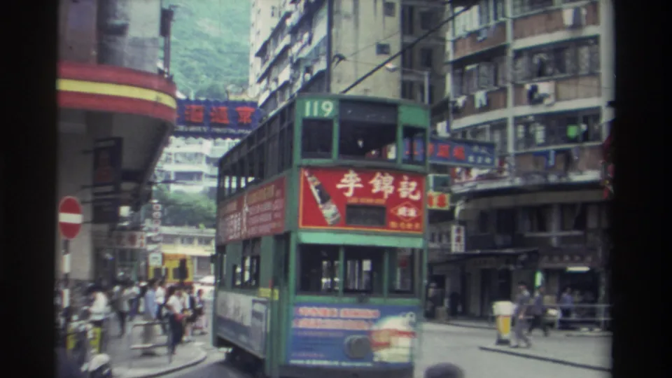 Route 119 green double-decker tram navigating a busy Hong Kong street in 1982, with a red Chinese-character advertisement panel and high-rise residential buildings behind.