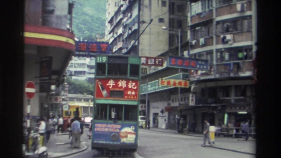 Close view of a route 119 green double-decker tram in 1982 Hong Kong, with a bold red Chinese-language advertisement and multiple layers of commercial signage on surrounding buildings.