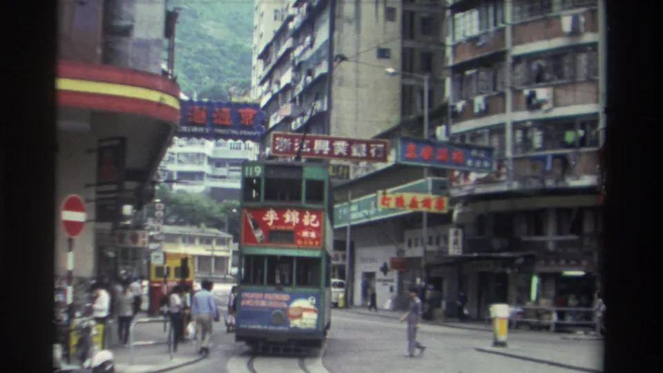 A 1982 Hong Kong street view showing the route 119 tram, foreground pedestrians in period clothing, and dense Chinese-character commercial signage lining mid-rise and high-rise buildings.