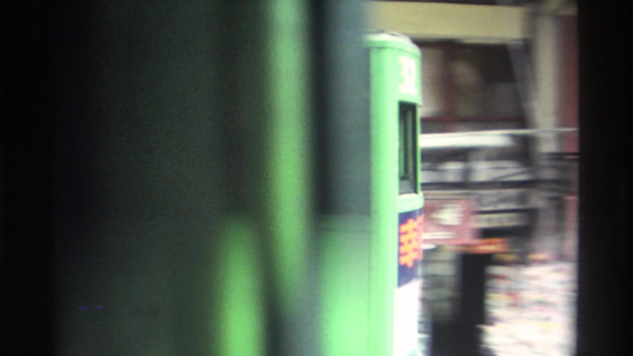 Circa 1982 Hong Kong: extreme close-up of a green double-decker tram caught through a vehicle window, with dark frame vignetting, motion blur, and partial Chinese signage on the tram body.