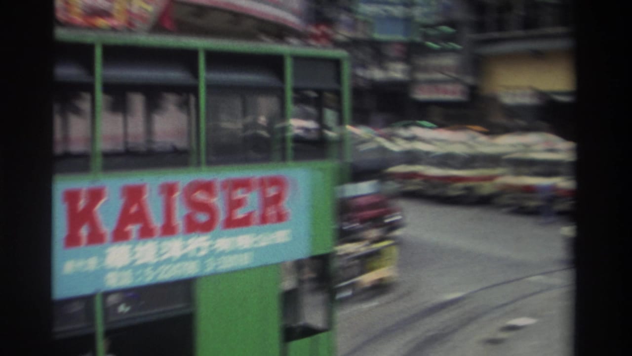 Green double-decker tram with a large blue KAISER advertisement in red lettering and Chinese characters, surrounded by moving street traffic and tram tracks.