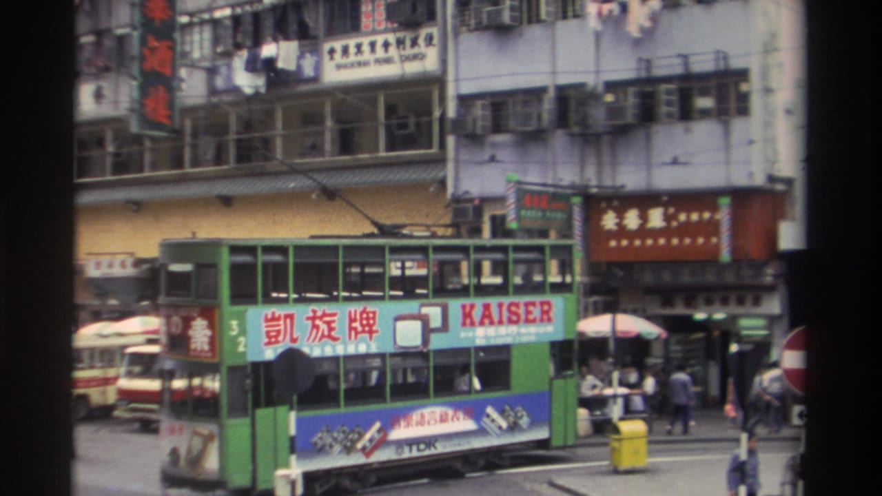 Green double-decker tram bearing a bilingual Kaiser TV advertisement passes through a busy Hong Kong street in 1982, framed by a characteristic 8mm film border.