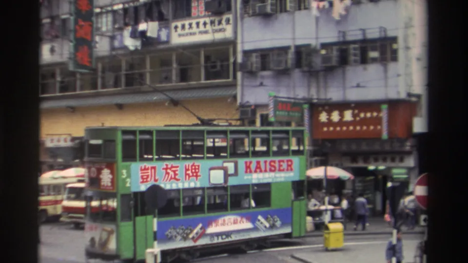 Green double-decker tram bearing a bilingual Kaiser TV advertisement passes through a busy Hong Kong street in 1982, framed by a characteristic 8mm film border.