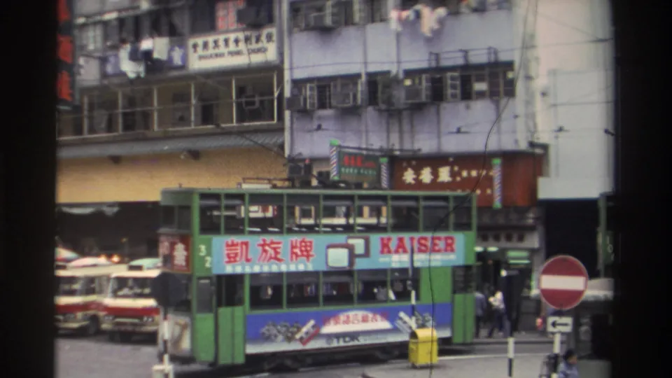 Green double-decker tram with bilingual Kaiser ad on a busy Hong Kong street in 1982; a red circular no-entry road sign is visible at right.