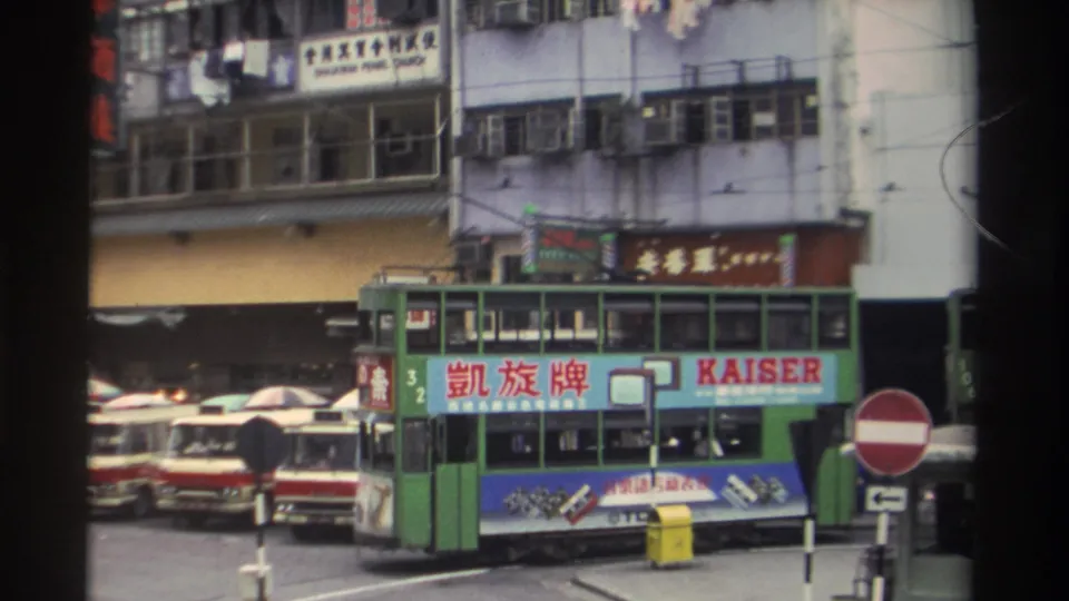 Green double-decker tram bearing Kaiser bilingual ad panel at closer range on a 1982 Hong Kong street; red no-entry sign visible at lower left.
