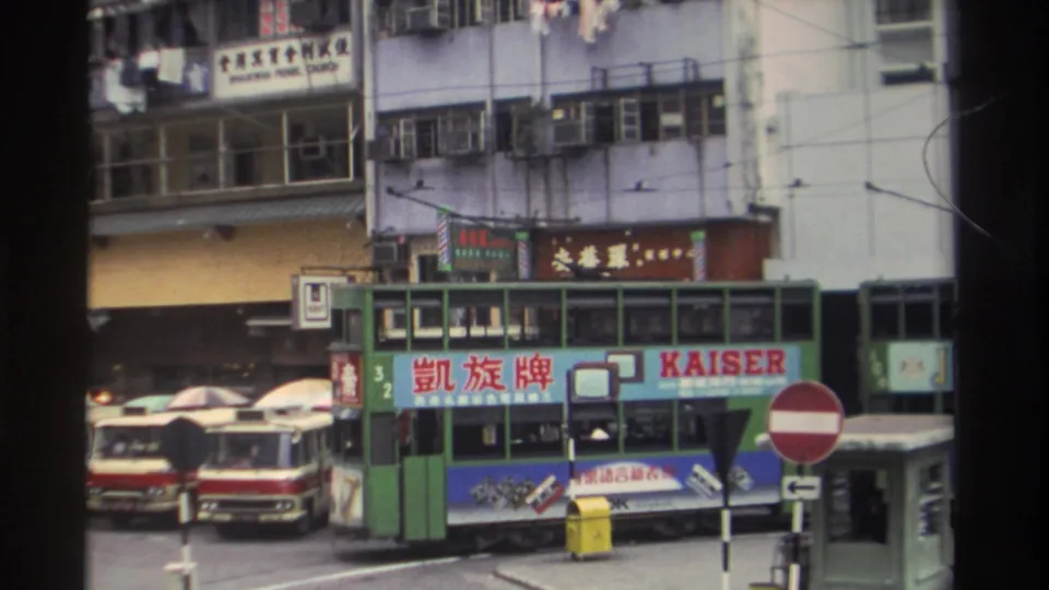 Green double-decker tram with Kaiser/凱旋牌 advertisement on a 1982 Hong Kong commercial street; multi-storey buildings dense with Chinese signage rise above.