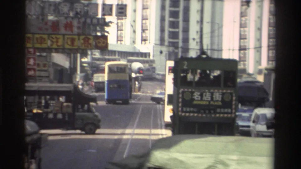 Closing frame of 8mm Hong Kong tram sequence circa 1982: route-2 tram with Chinese characters advances through dense traffic beneath commercial banner signage on both sides.