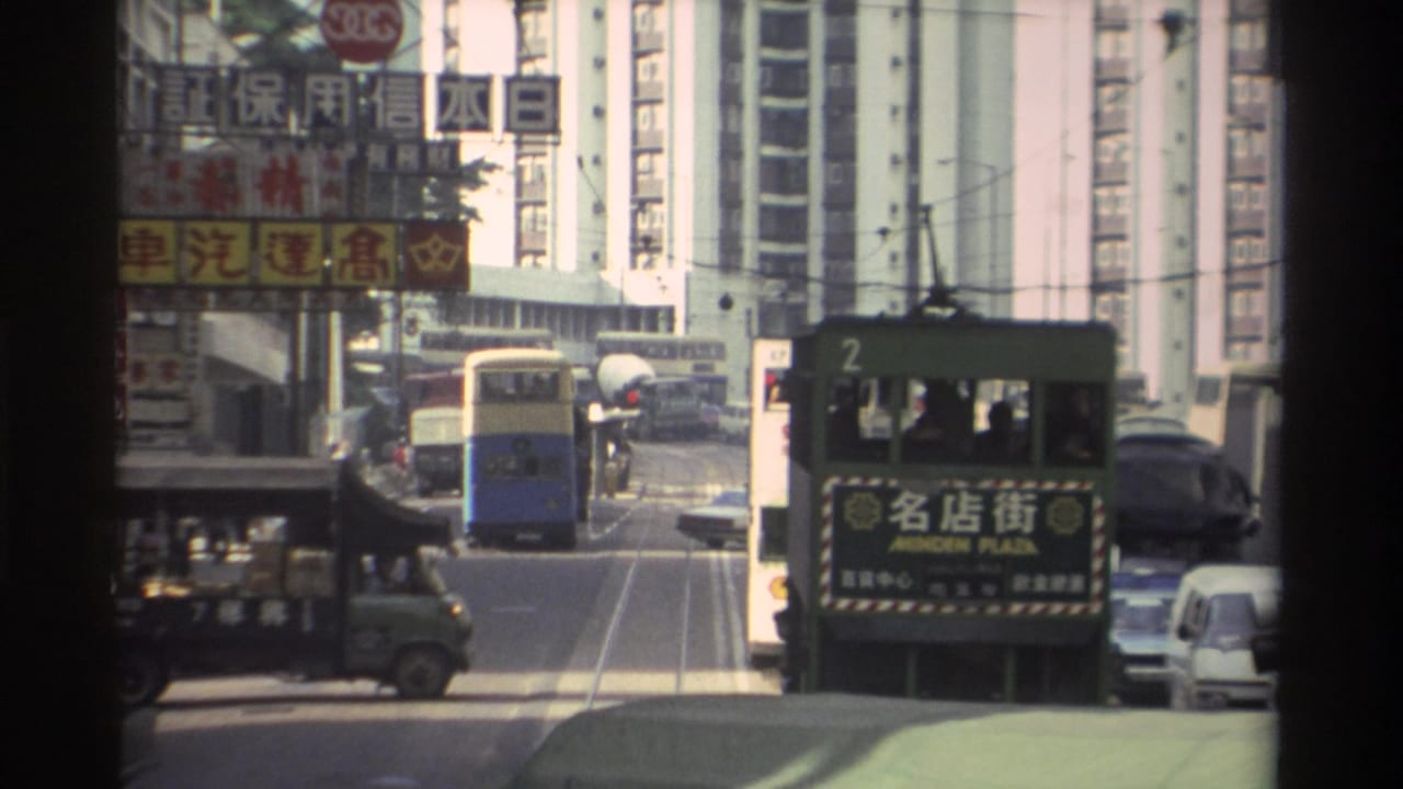 Green double-decker tram numbered 2 with Minden Plaza destination sign on a Hong Kong street, with a blue bus, green delivery truck, and Chinese commercial billboards visible.