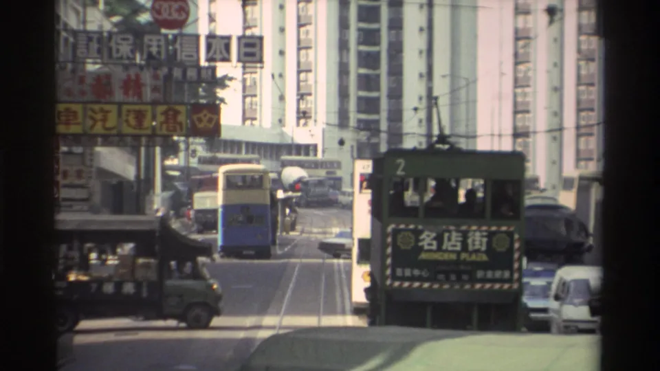 Green double-decker Hong Kong tram (route 2, Minden Plaza) on a tram corridor in 1982, flanked by a blue bus, green delivery truck, and tower blocks hung with Chinese-language billboards.
