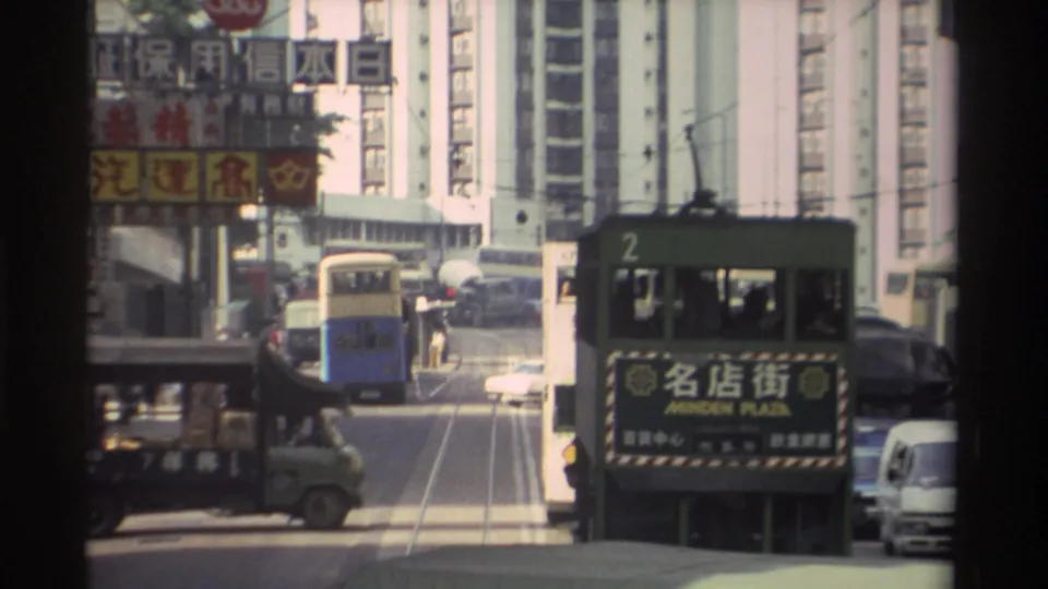 Green double-decker tram numbered 2 heading to Minden Plaza moves through a 1982 Hong Kong street lined with Chinese commercial signage, a blue bus, and high-rise buildings.
