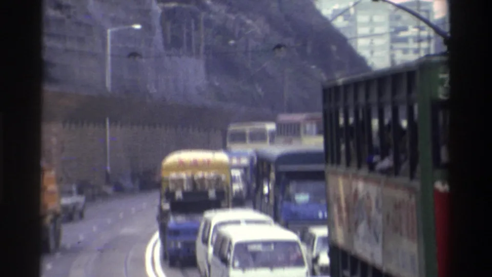 Hong Kong tram no. 36 viewed from an adjacent vehicle amid mixed traffic, rocky hillside visible, circa 1982, 8mm film.