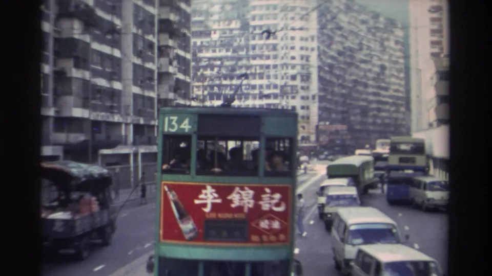Close approach of Hong Kong tram route 134 showing the red Lee Kum Kee (李錦記) advertisement panel prominently, flanked by vans and trucks, high-rise towers behind, circa 1982.