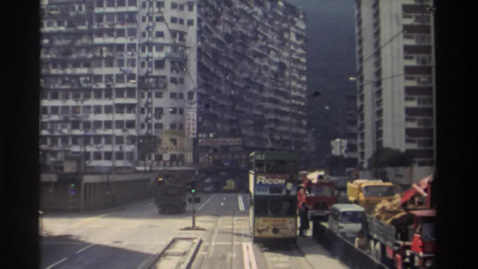 1982 Hong Kong street scene showing tram 162 with a Ricoh advertisement panel, dense residential tower blocks, yellow construction machinery, and mixed traffic on tram tracks.