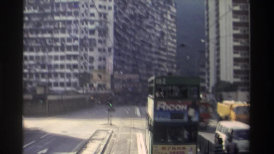 Final 8mm frame from 1982 Hong Kong showing tram 162 with Ricoh advertisement, a yellow construction crane on the right margin, and a wall of residential high-rises under clear sky.