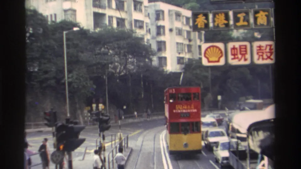 Hong Kong, c.1982: tram with visible route markings advances toward camera; Shell Chinese-language sign and commercial signage overhead; traffic lights in foreground.