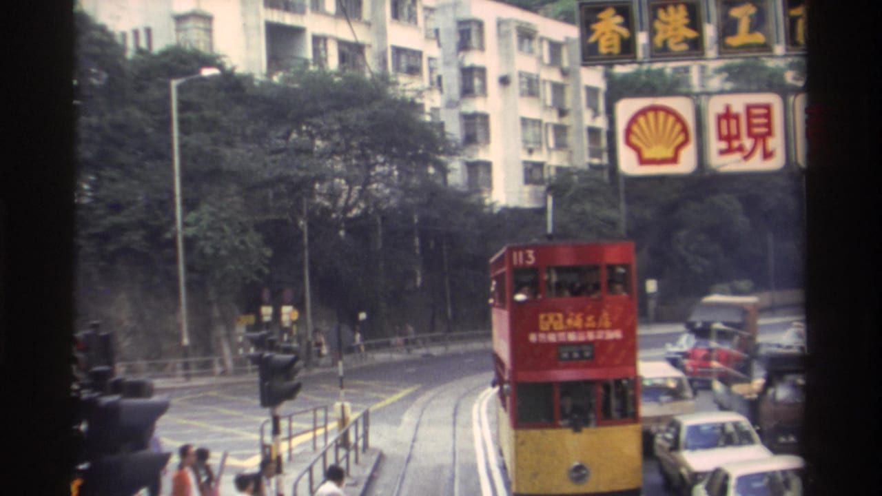 Hong Kong double-decker tram numbered 113 rounding a curve, Shell hoarding and Chinese-language billboards in background, pedestrians on pavement, circa 1982, 8mm film.