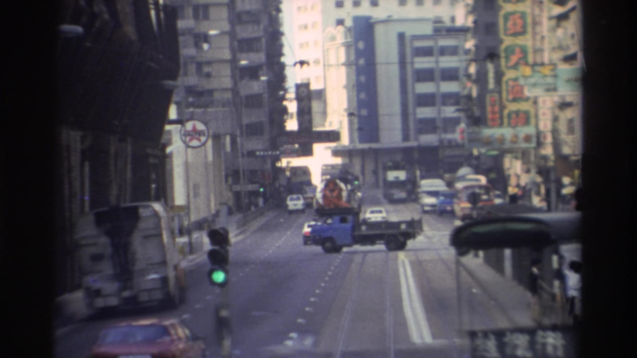 Tram's forward view on a Hong Kong street showing a blue flatbed utility truck, mixed traffic, Chinese-character signs on tall buildings, and a green traffic light.