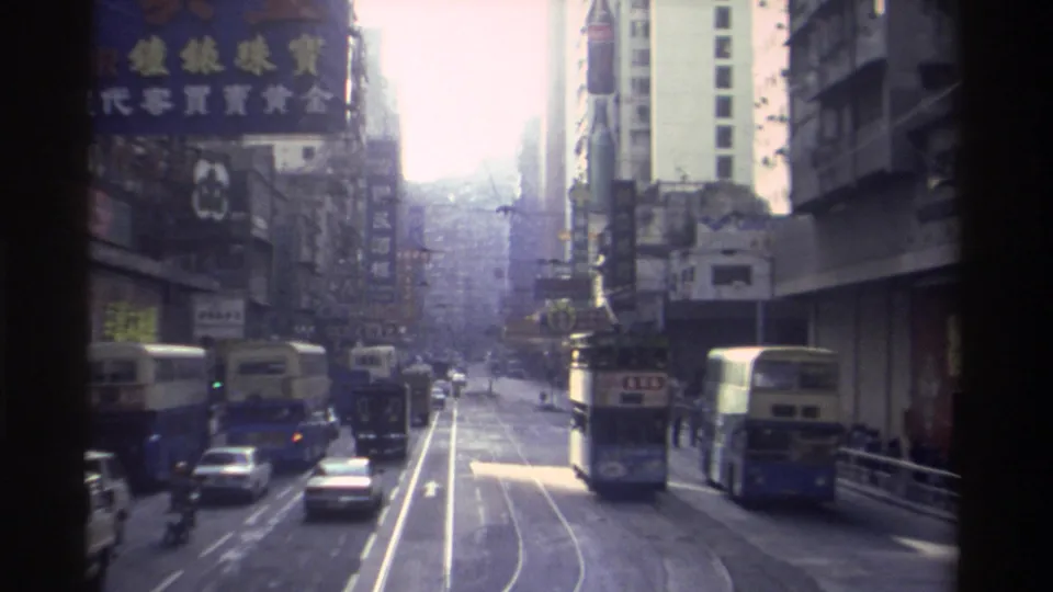 8mm view of a Hong Kong commercial thoroughfare circa 1982, with trams on both sides, Chinese-language advertising signs, and overexposed sky at the far end of the street.