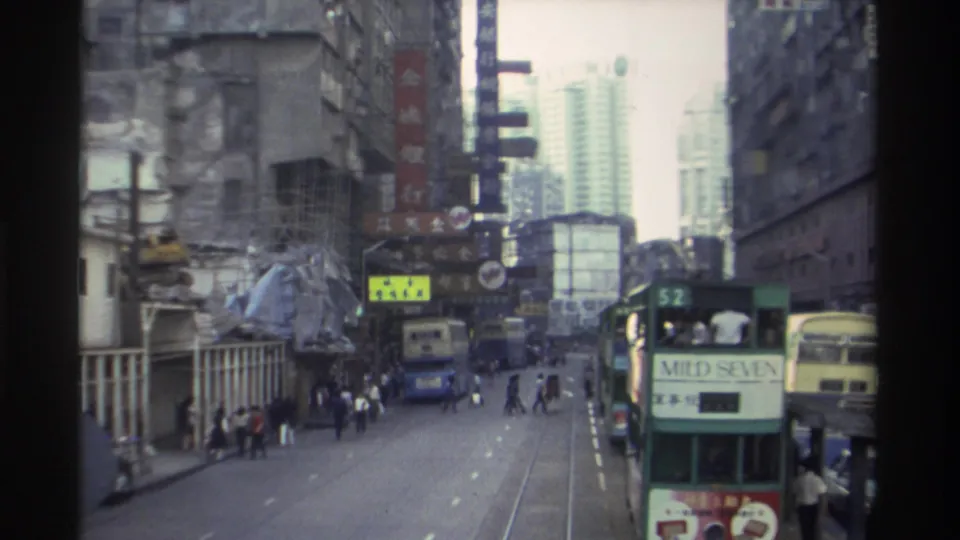 1982 Hong Kong street scene — trams on tracks including one advertising Mild Seven, dense Chinese commercial signage, mid-rise and high-rise buildings.