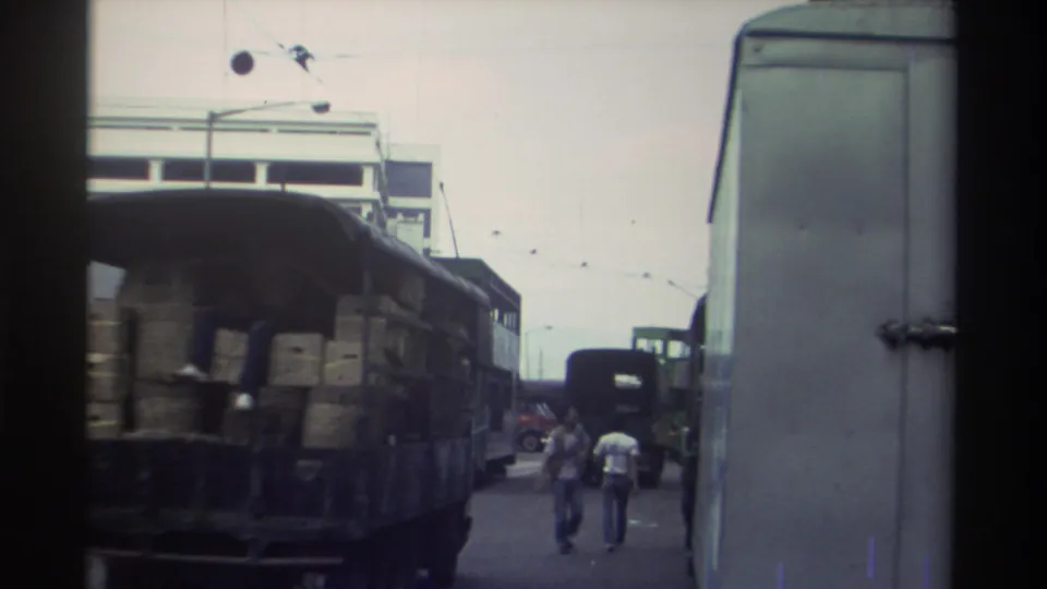 1982 Hong Kong — open flatbed truck loaded with cargo crates, green trams and pedestrians behind, overhead tram wires above the street.