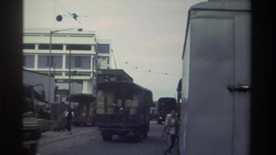 Slightly shifted angle of the same Hong Kong commercial street circa 1982 shows the crate-loaded truck and a pedestrian more clearly, with a numbered building facade visible behind.