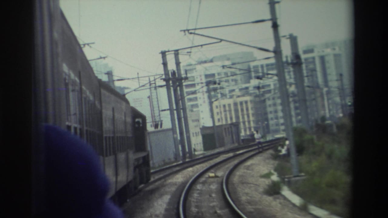Passenger's view from a moving train in Hong Kong, c. 1982, showing curved tracks, catenary overhead wires, and mid-rise apartment blocks.
