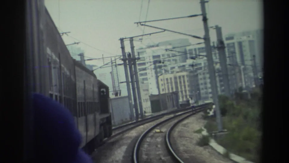 Passenger's view from a moving train in Hong Kong, c. 1982, showing curved tracks, catenary overhead wires, and mid-rise apartment blocks.