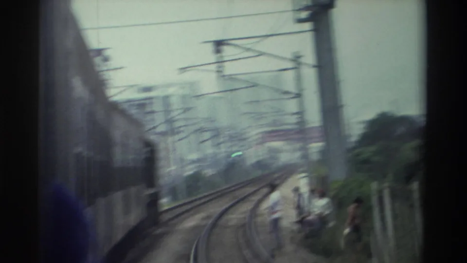 Final frame from the Hong Kong light rail sequence, c. 1982, with heavy motion blur across tracks, wires, and trackside people.