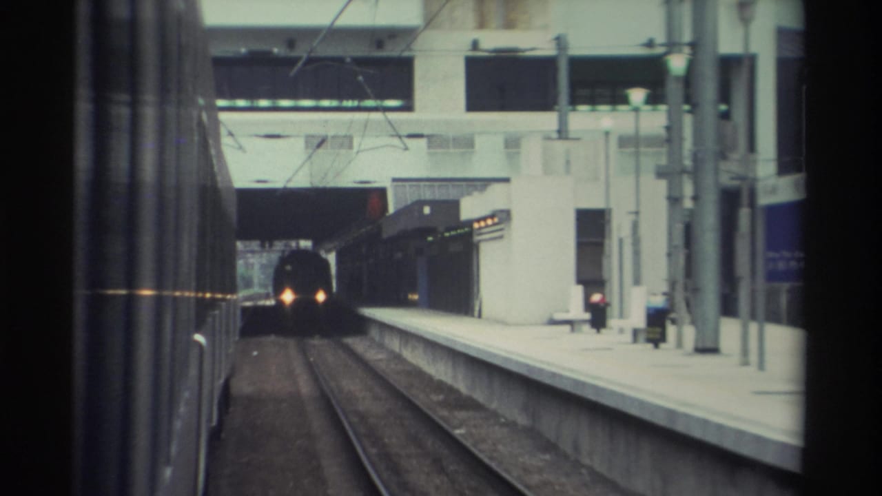 8mm home movie frame, 1982 Hong Kong: POV from a train window looking along a concrete platform as another train approaches with lit headlights.