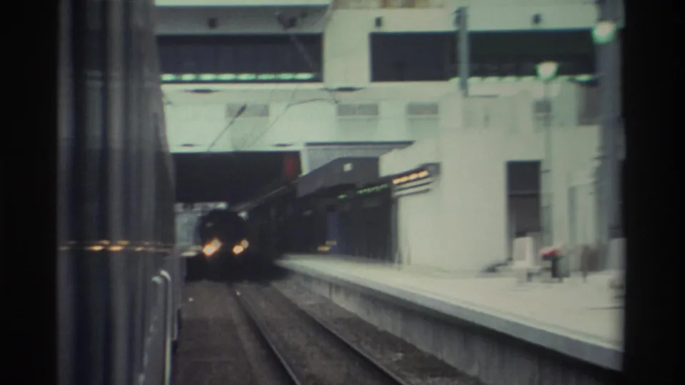 8mm frame, 1982 Hong Kong: a train bears down the track toward the camera position, the platform and blue-paneled station wall visible at right.