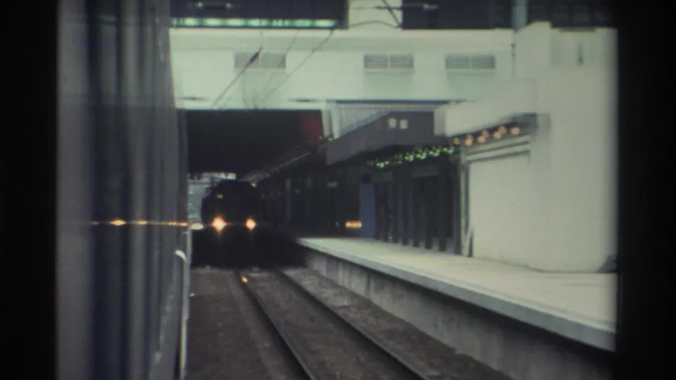 8mm frame, 1982 Hong Kong: platform canopy fitted with a row of green signal lights frames an oncoming train still distant near the tunnel mouth.