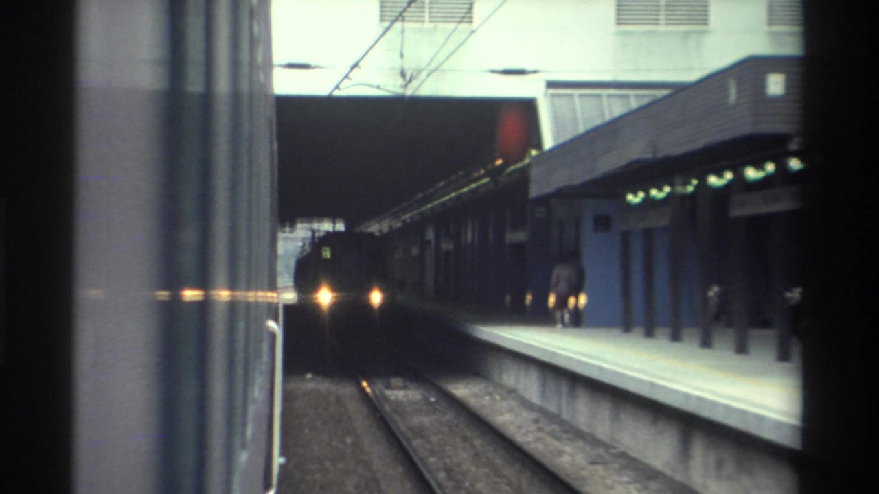 8mm home movie frame showing an approaching train at a covered rail station platform, likely Hong Kong, circa 1982.