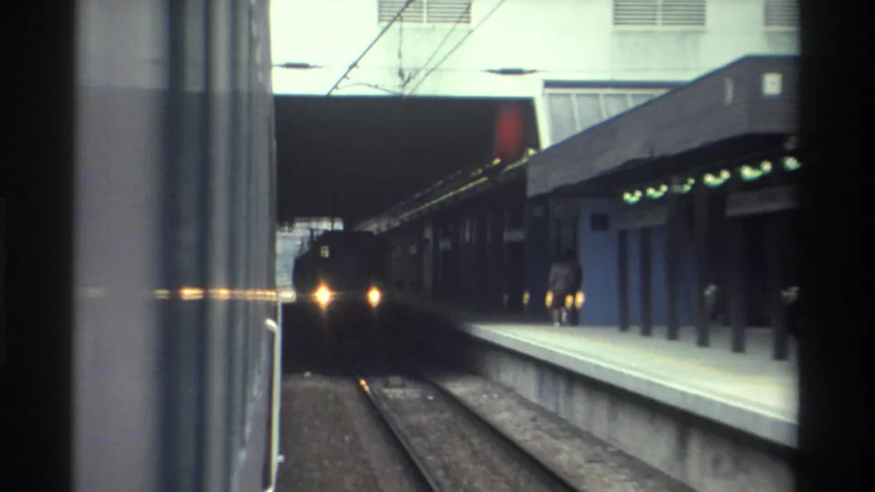 8mm home movie frame showing an approaching train at a covered rail station platform, likely Hong Kong, circa 1982.