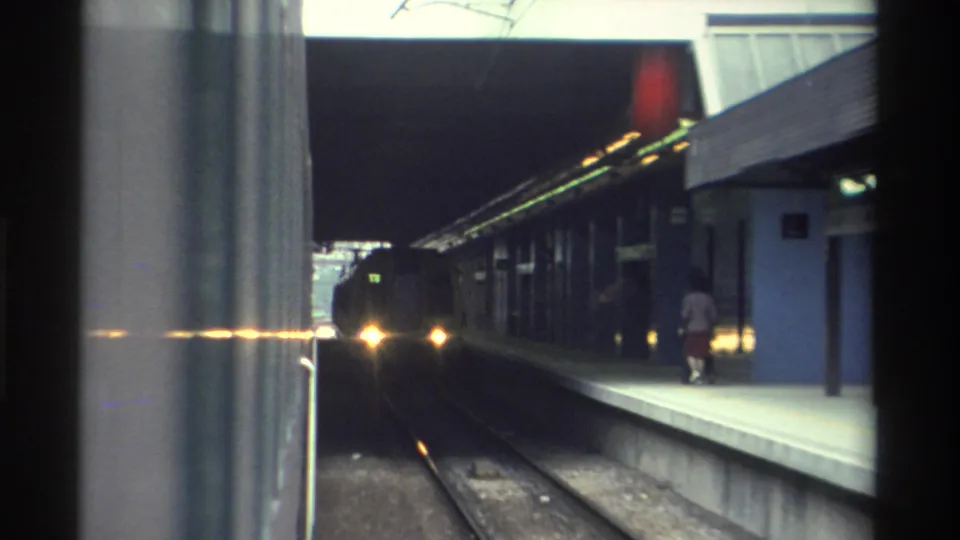 8mm home movie of an approaching train and silhouetted passengers under a covered station canopy, likely Hong Kong rail, circa 1982.