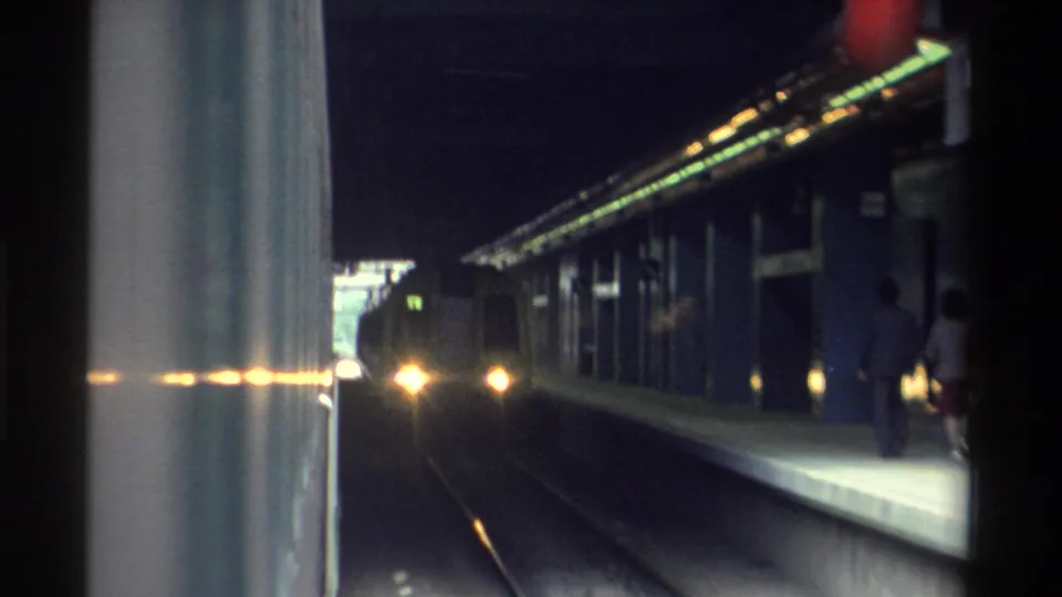 8mm home movie frame showing a station scene darkening as the camera nears a shaded section, with a lone figure on the platform, likely Hong Kong, 1982.