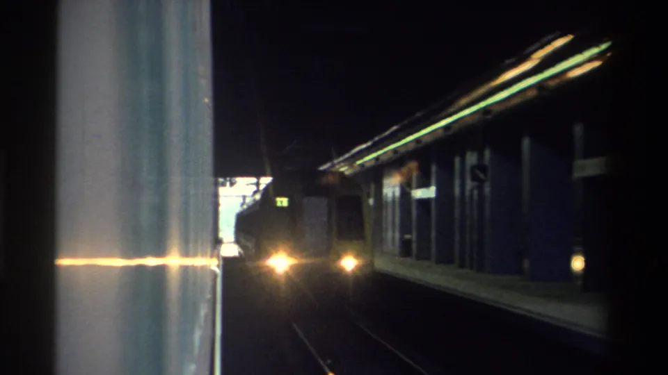 8mm home movie frame capturing a train headlight cutting through tunnel darkness as the station scene recedes, likely Hong Kong, 1982.