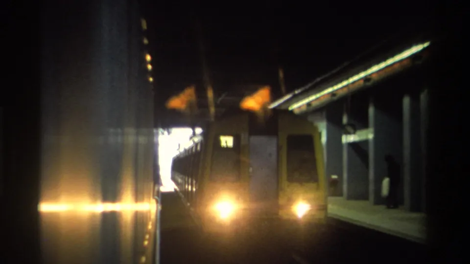 8mm footage of a Hong Kong train with headlights blazing as it moves through a tunnel, c. 1982; yellow-green car body and platform wall visible alongside.