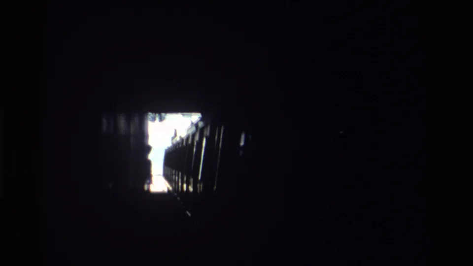 Interior of a Hong Kong railway tunnel, circa 1982, looking toward the bright tunnel exit with a train silhouette in deep shadow.