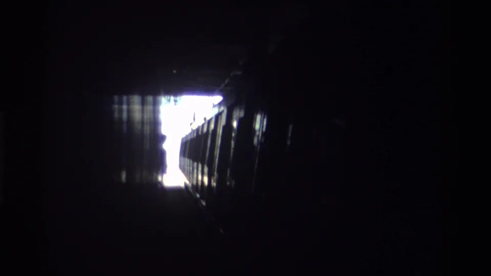 Hong Kong railway tunnel interior, circa 1982, showing the overexposed exit and train carriage edges advancing through deep shadow.