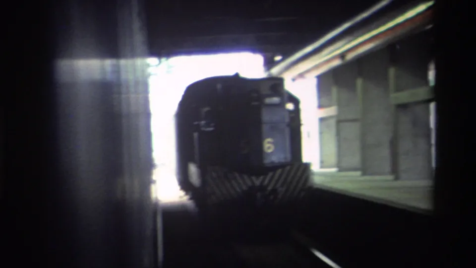 Hong Kong railway locomotive numbered 6 in yellow on its front, emerging from a tunnel toward a station platform, filmed on 8mm circa 1982.