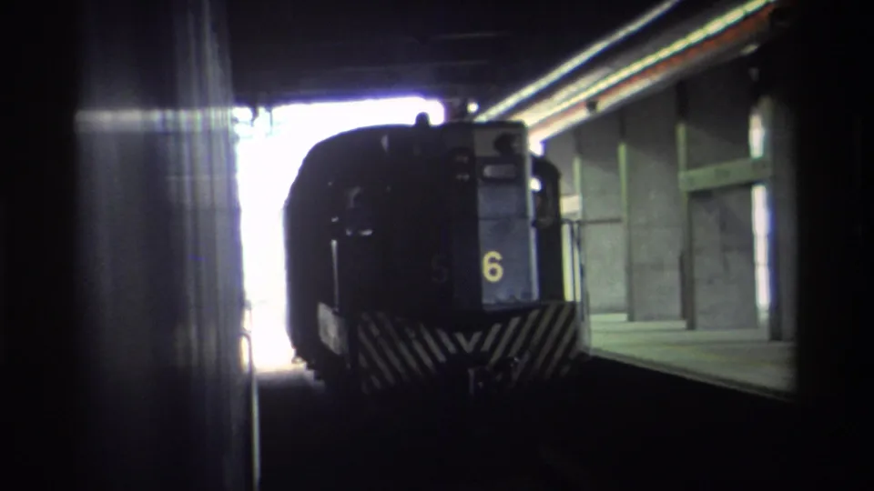 Hong Kong, 1982 — dark blue train numbered 6 with diagonal chevron markings seen from a covered station platform, captured on 8mm home movie film.