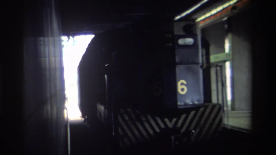 Hong Kong, 1982 — locomotive front with yellow numeral 6 and diagonal safety chevrons, 8mm film showing exposure contrast between dark station interior and bright exterior.